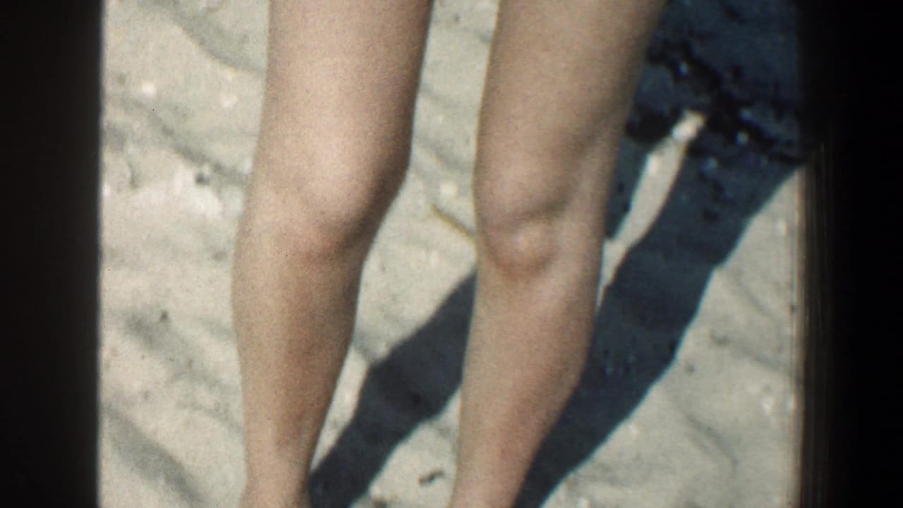 Bare legs of a young woman standing on sandy beach.