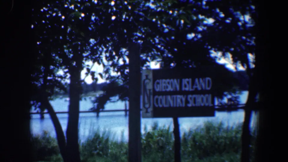 1961 Maryland frame showing a Gibson Island Country School sign by trees with water visible in the background.