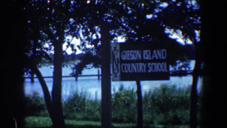1961 8mm view of a Gibson Island Country School sign framed by trees near the Maryland shoreline.