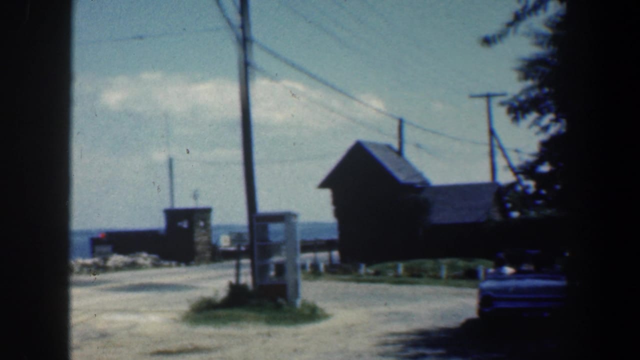 Roadside view with phone booth, small wooden building, utility poles, and water in the distance.
