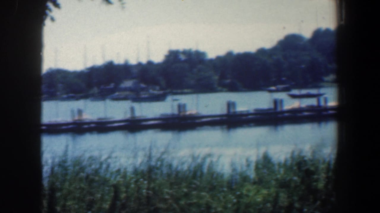 1961 Baltimore-area 8mm frame showing a dock and small boats across calm water, seen through dark window edges.