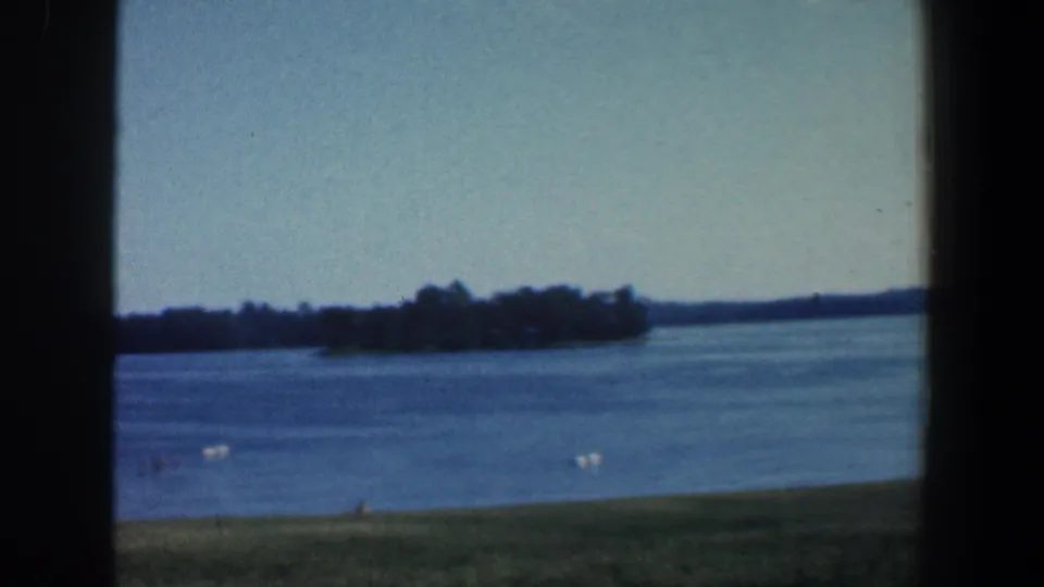 1961 Baltimore-area home-movie frame of a blue lake and distant tree-covered land, partly divided by a dark window or door frame.