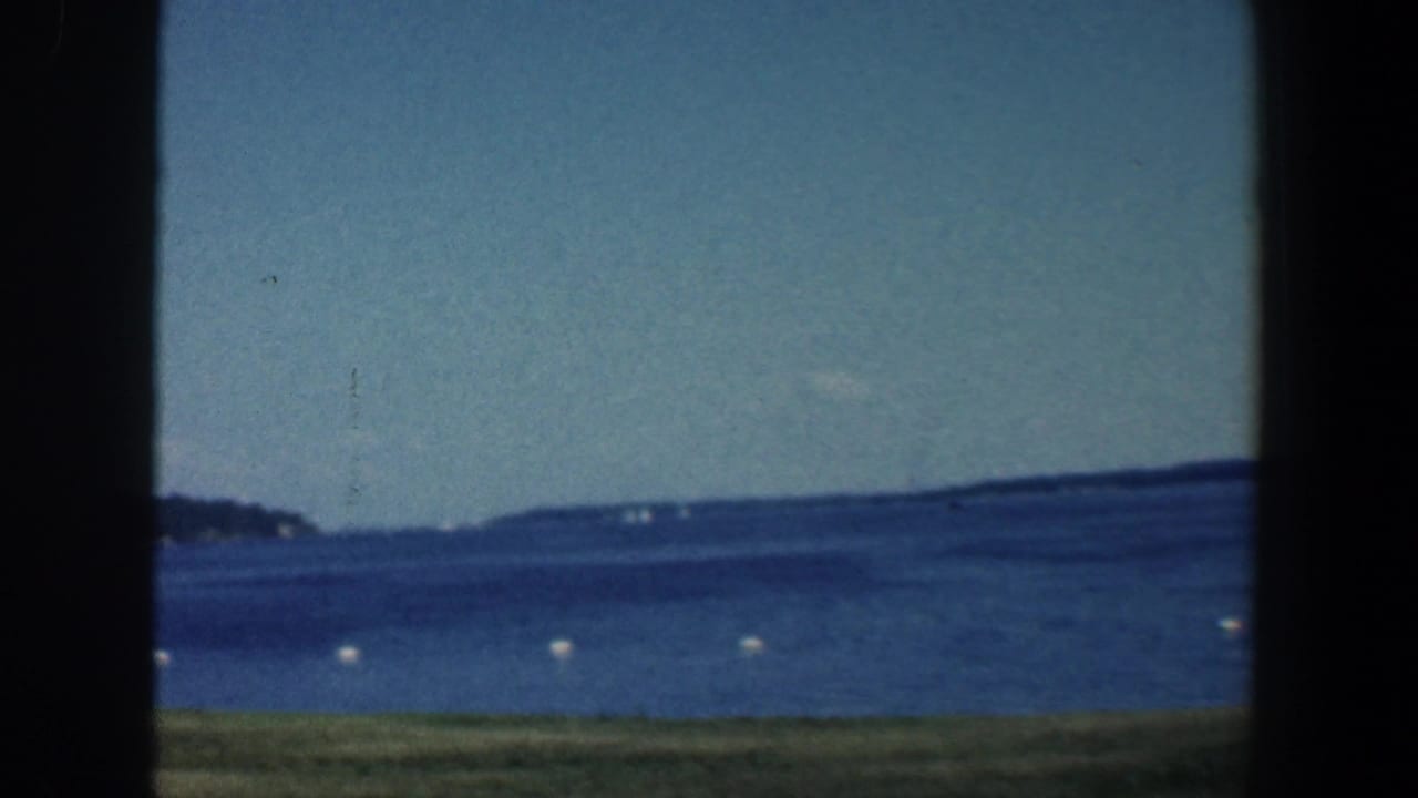 Wide blue water with white buoys, distant hills, and dark window-like borders.