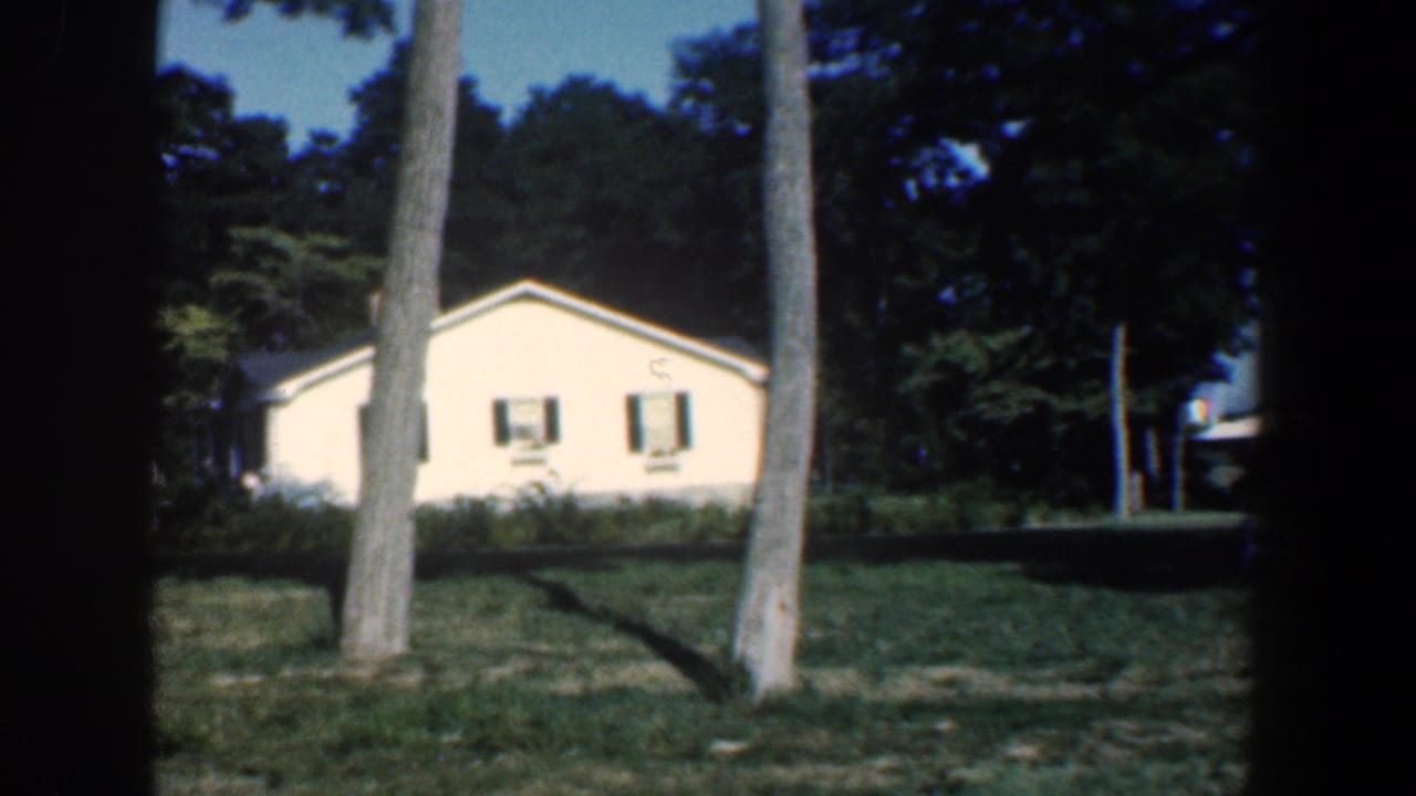 1961 Baltimore-area 8mm frame showing a pale house among tall trees and a grassy yard.