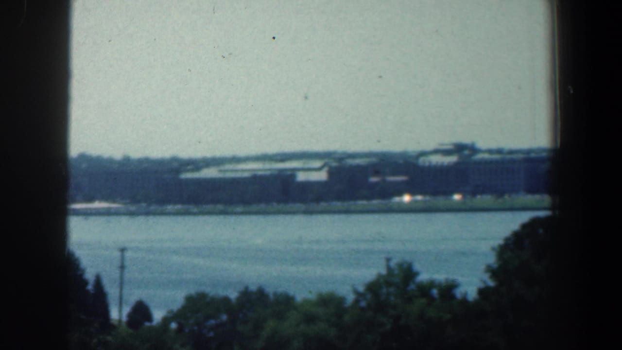 Wide river with distant low buildings and dark vertical framing in the foreground.
