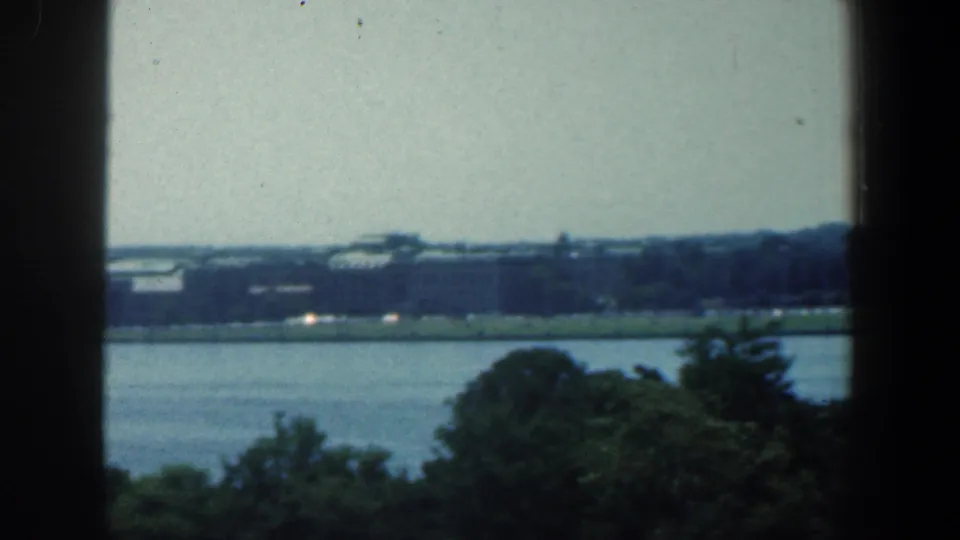 A soft 8mm view of Baltimore's distant riverfront, showing trees below the camera and low buildings along the opposite bank.