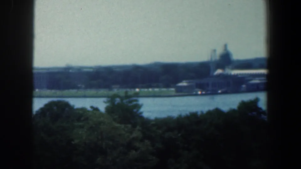 1961 Baltimore river view with foreground trees, distant waterfront buildings, smokestacks, and a domed structure near the right side.