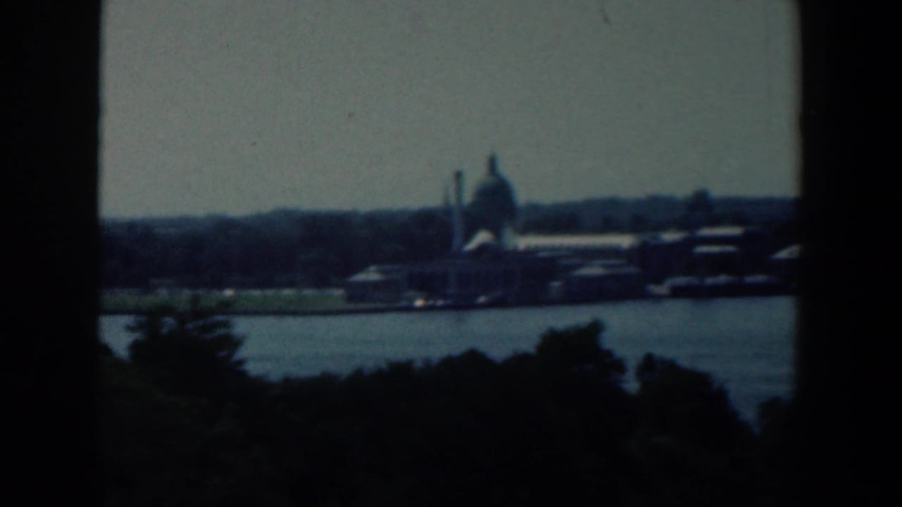 Distant waterfront buildings and a domed structure across blue water, framed by dark window edges.
