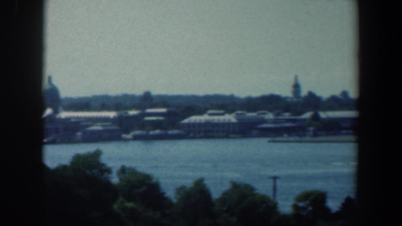 Wide water view with distant waterfront buildings, trees, and dark vertical window framing.