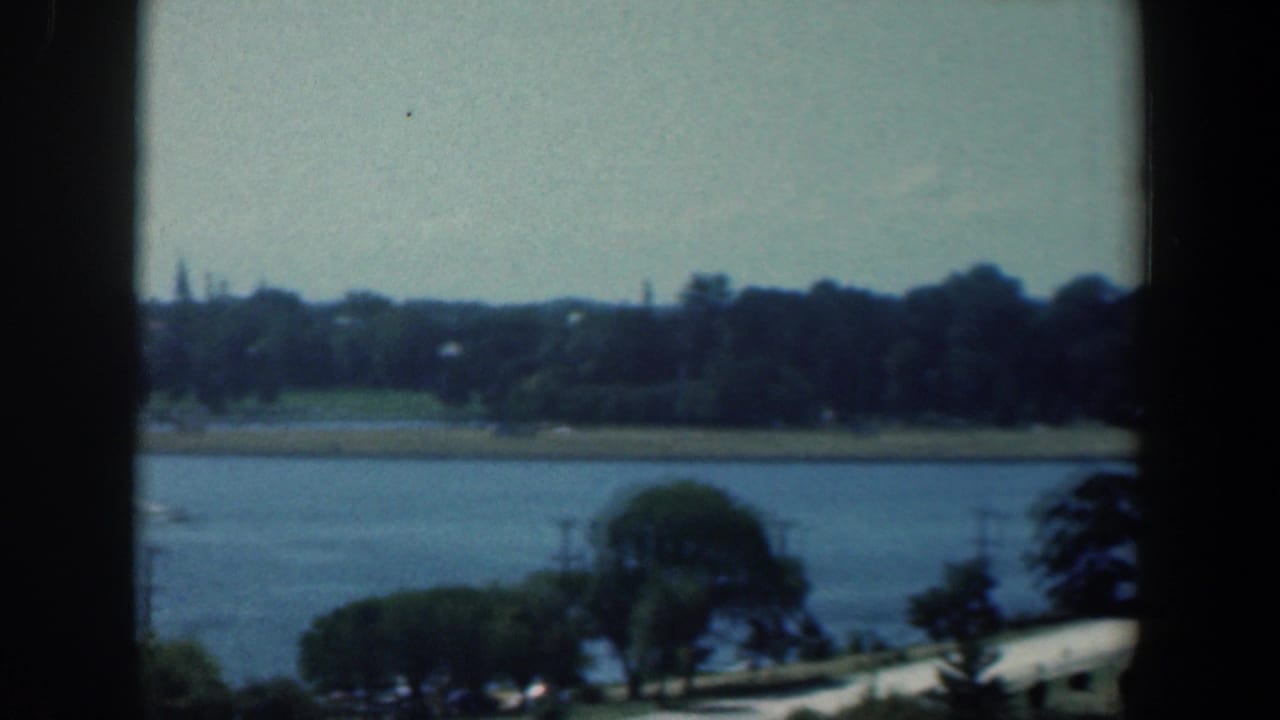 Waterway and tree-lined shore viewed through dark window framing.