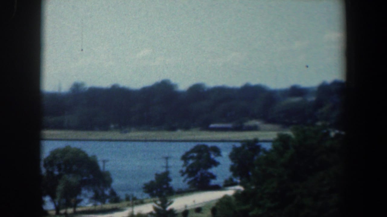 Waterfront landscape with trees, road, and distant shoreline through a window.