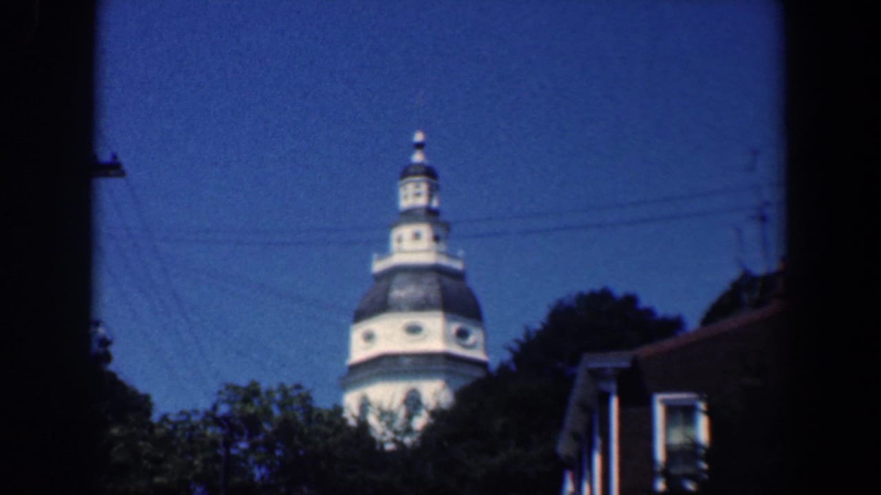 White domed tower above trees and wood-sided houses under a blue sky.