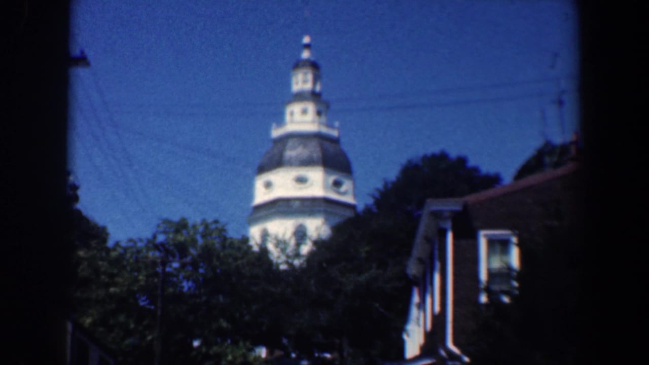 1961 Baltimore residential view with a white domed tower beyond trees, utility wires, and house rooflines.