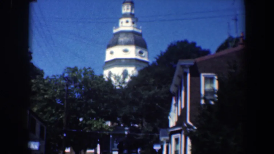 1961 Baltimore frame with wood-sided houses, green trees, and a white domed tower in the background.