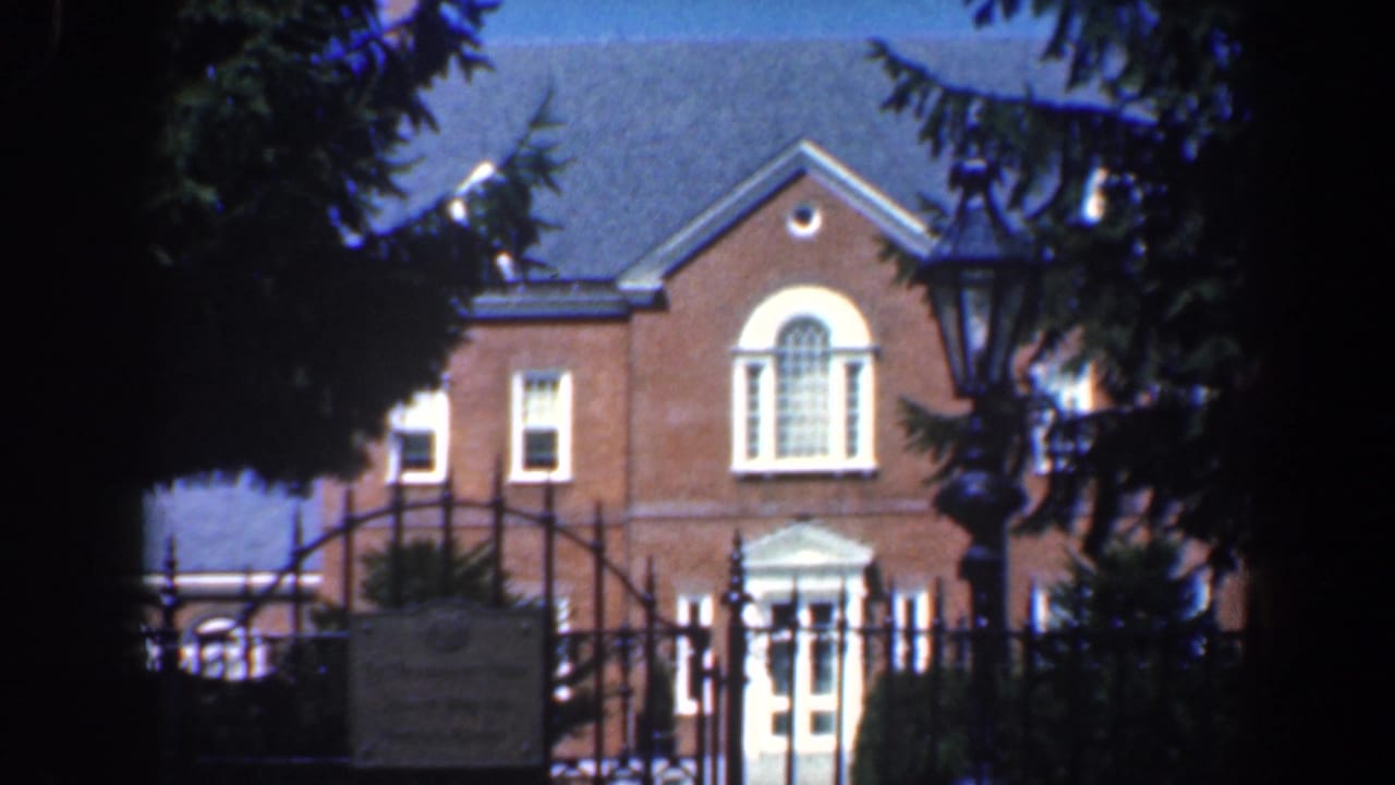 Brick building behind an iron gate, framed by trees and a lamppost.