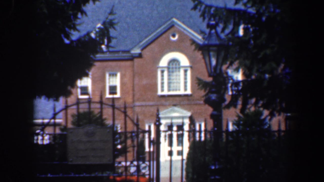 Iron gate and lamppost in front of a brick building with white trim.