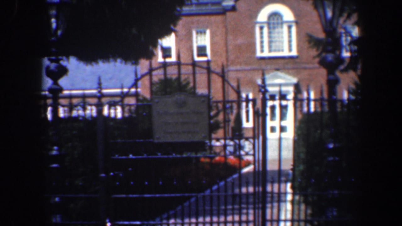 Brick house seen through a dark wrought-iron gate and trees.