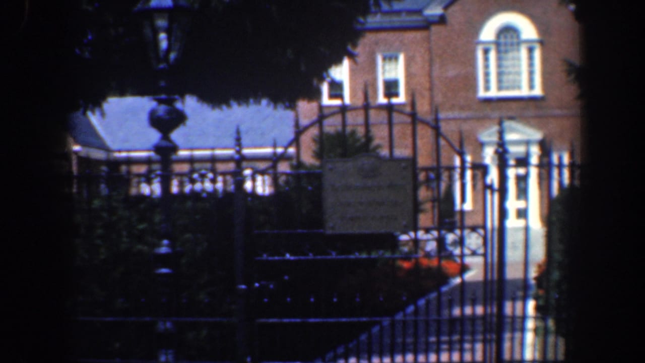 Brick house facade behind a wrought-iron gate and shaded trees.