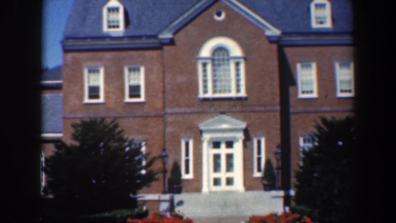 Closer view of brick facade with arched window, white doorway, shrubs, and flowers.