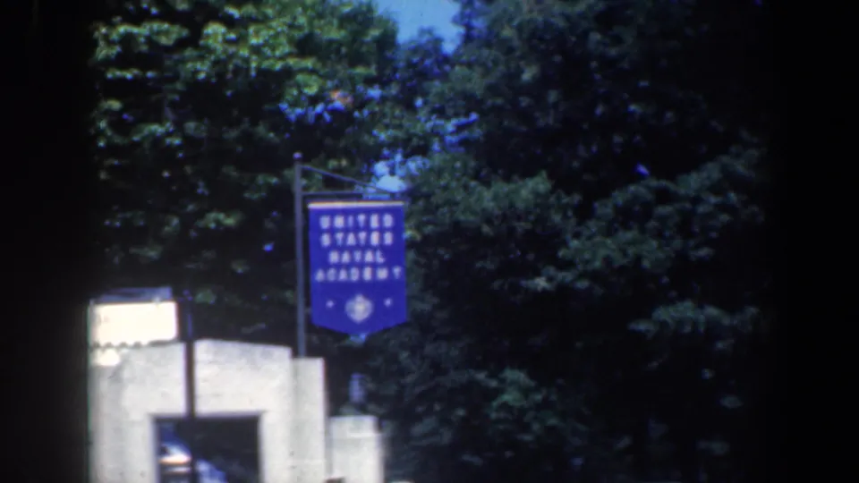 1961 Maryland 8mm frame showing a blue United States Naval Academy banner beside trees and a low exterior structure.