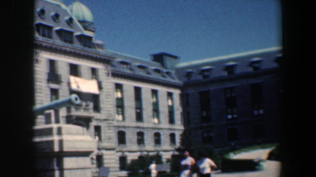 Stone civic building with a cannon monument in front under a blue sky.