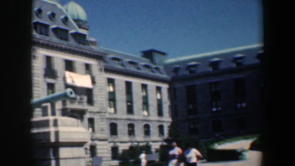 1961 Baltimore 8mm frame showing a stone civic building, mansard roof, green dome, and cannon monument with visitors nearby.