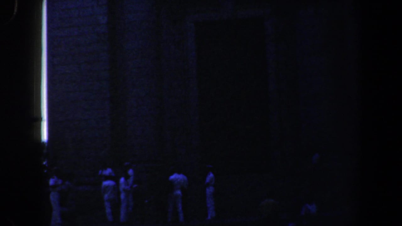 Small group in white stands outside a dark brick church at night.