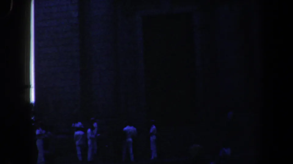 1961 Baltimore 8mm frame showing people in white near a brick church entrance under dark blue night exposure.