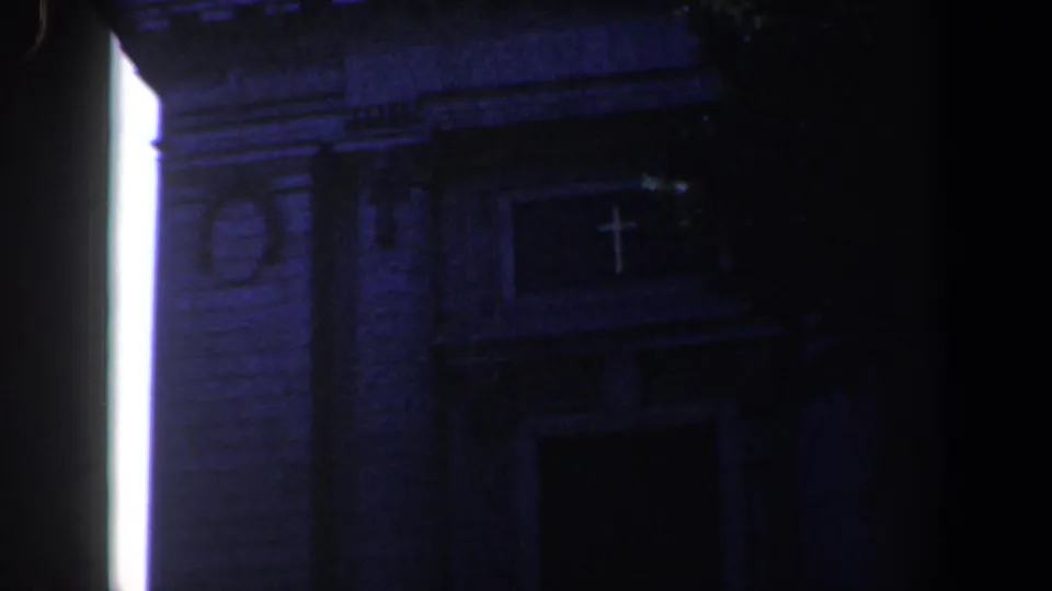 1961 Baltimore 8mm frame showing a shaded stone church facade with a cross above the entrance and bright sky at the side.
