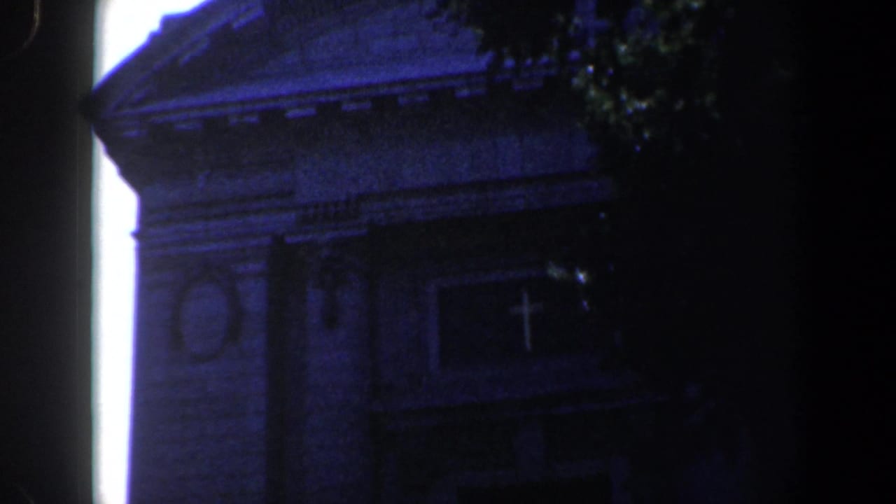 Upper church facade with pediment, cross detail, and leafy shade at right.