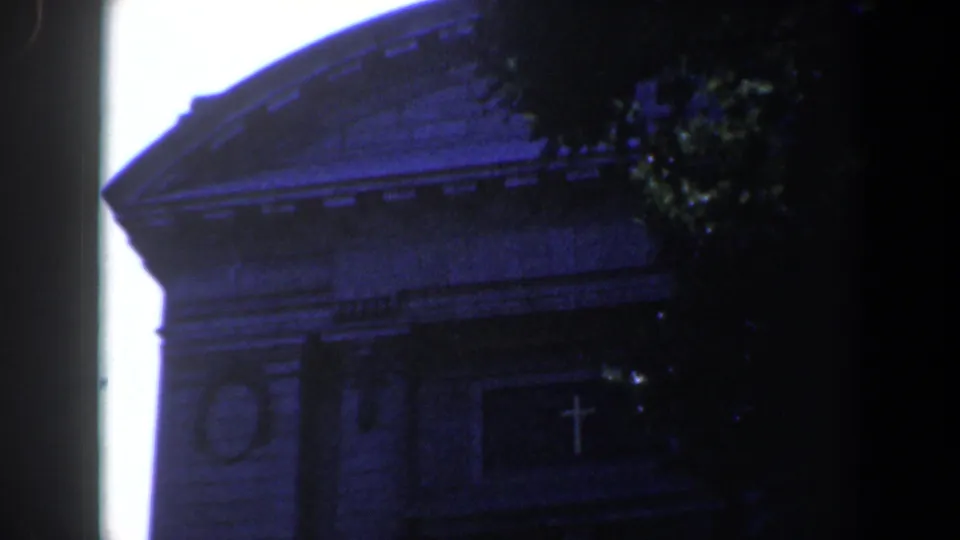 1961 Baltimore 8mm frame showing the church roofline, circular wall detail, and cross over the entrance in heavy blue-toned shade.