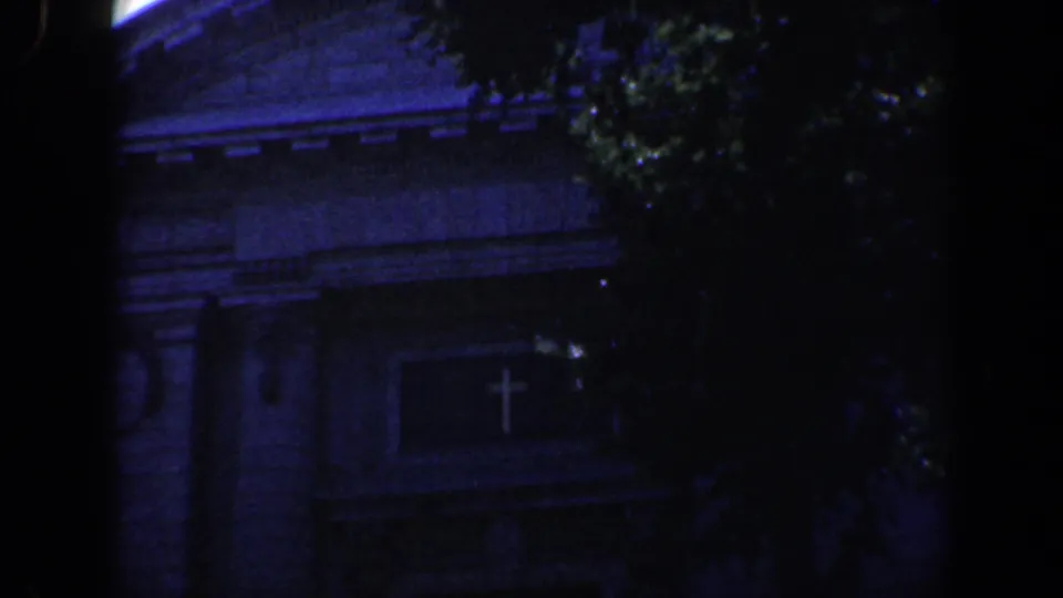 1961 Baltimore 8mm frame showing a shaded masonry building behind trees, with a cross-shaped emblem on the facade.