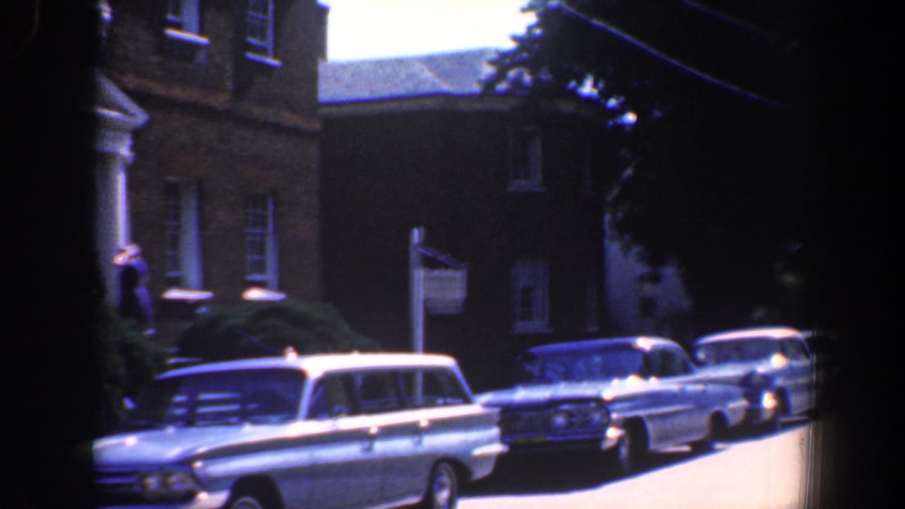 Parked vintage cars line a street beside a brick building with a white entrance.
