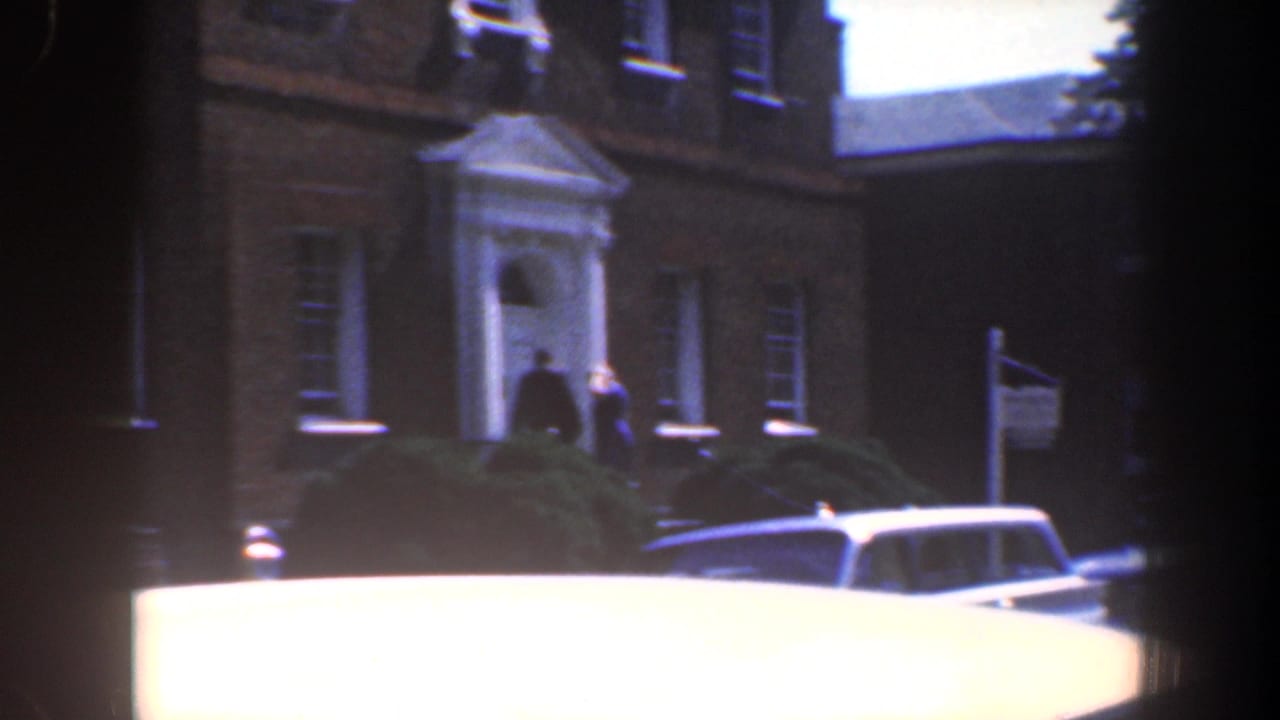 Brick building entrance with people near the doorway and a car roof in the foreground.