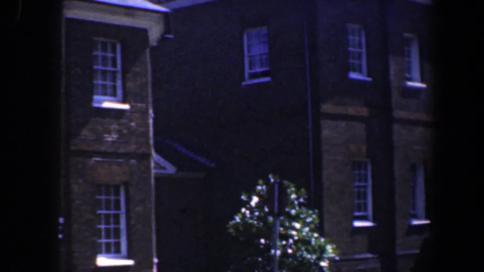 Soft 8mm view of a Baltimore brick building facade with sash windows, shrubbery, and a partial white entry canopy.