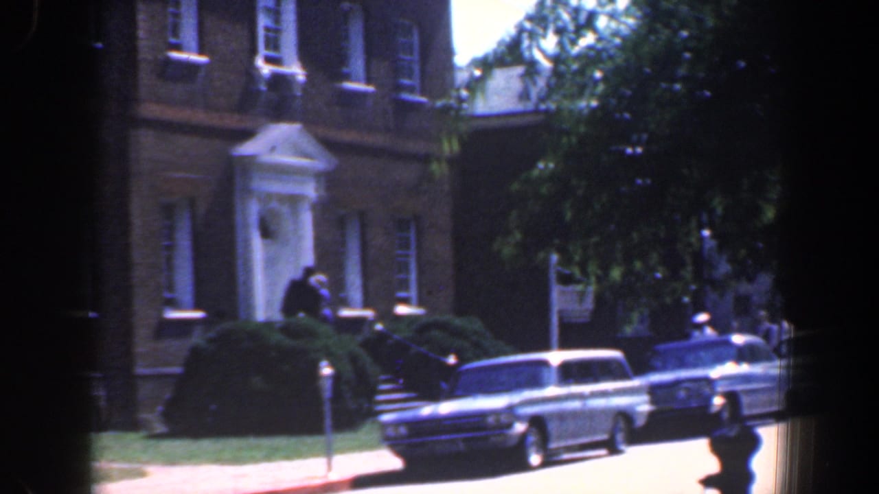Brick building facade, shrubs, parked station wagon, and a person near the sidewalk.