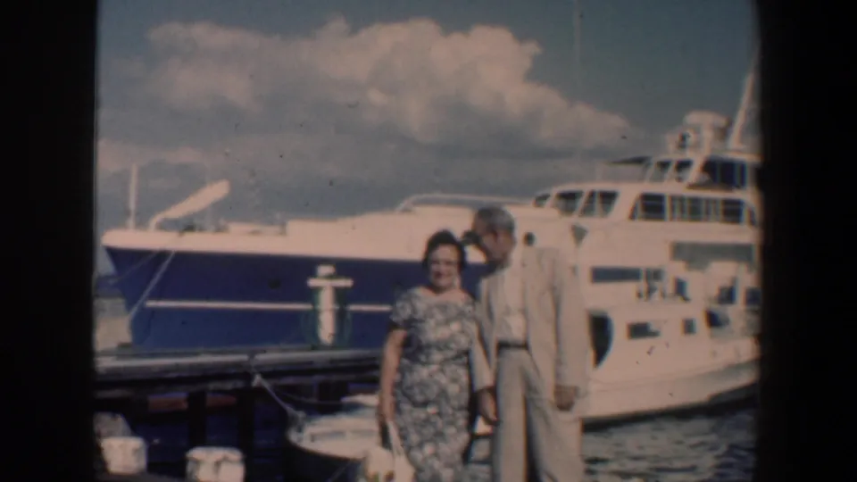 The couple remains posed at the Baltimore waterfront beside the white yacht, framed in soft 1961 8mm home-movie color.