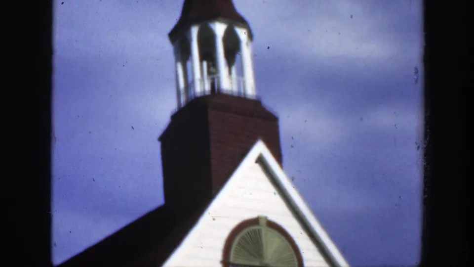 1950 Montreal home-movie frame showing a brown and white church bell tower with white columns and a pointed roof.