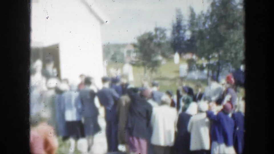 1950 Montreal home-movie frame showing people in mid-century clothing gathered outside a white church building.
