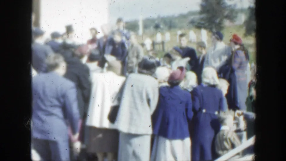 1950 Montreal wedding crowd viewed from behind, with suited men, women in hats, flowers, and trees in the background.