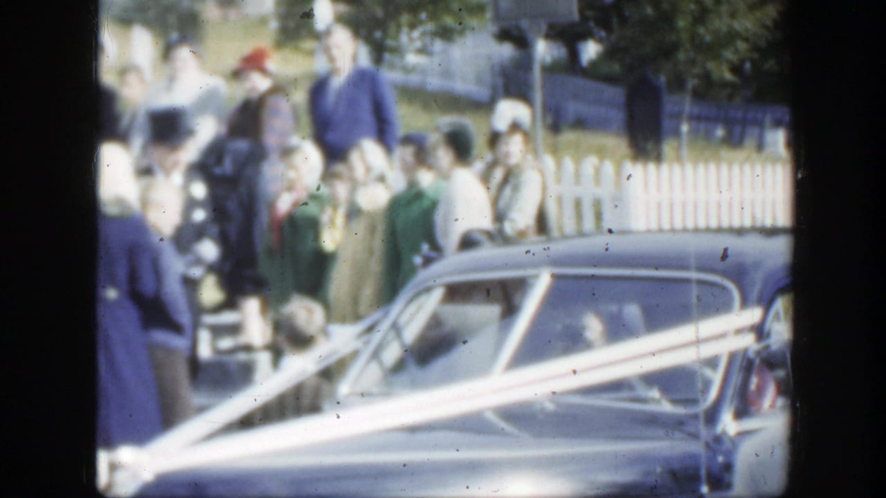Formal wedding guests in Montreal stand around a ribbon-trimmed car with trees and fencing behind them.