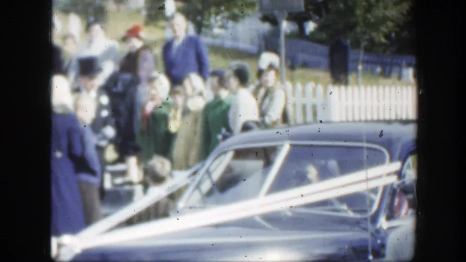 Formal wedding guests in Montreal stand around a ribbon-trimmed car with trees and fencing behind them.