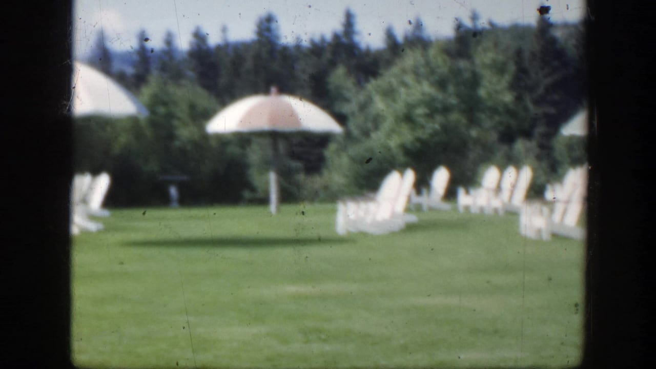 1950 Montreal 8mm view of white outdoor chairs and pale parasols arranged on a broad green lawn.