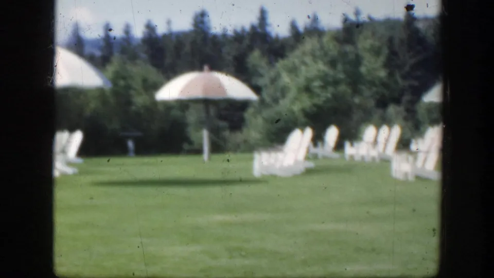 1950 Montreal 8mm view of white outdoor chairs and pale parasols arranged on a broad green lawn.