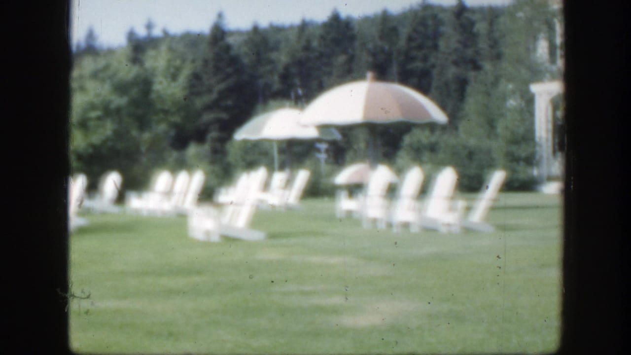 Manicured lawn with white chairs, umbrellas, trees, and part of a large villa.