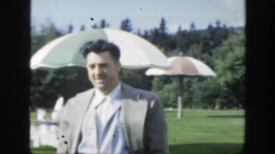A closer 1950 Montreal frame shows the man in a light suit and tie approaching beside a large umbrella on a green lawn.
