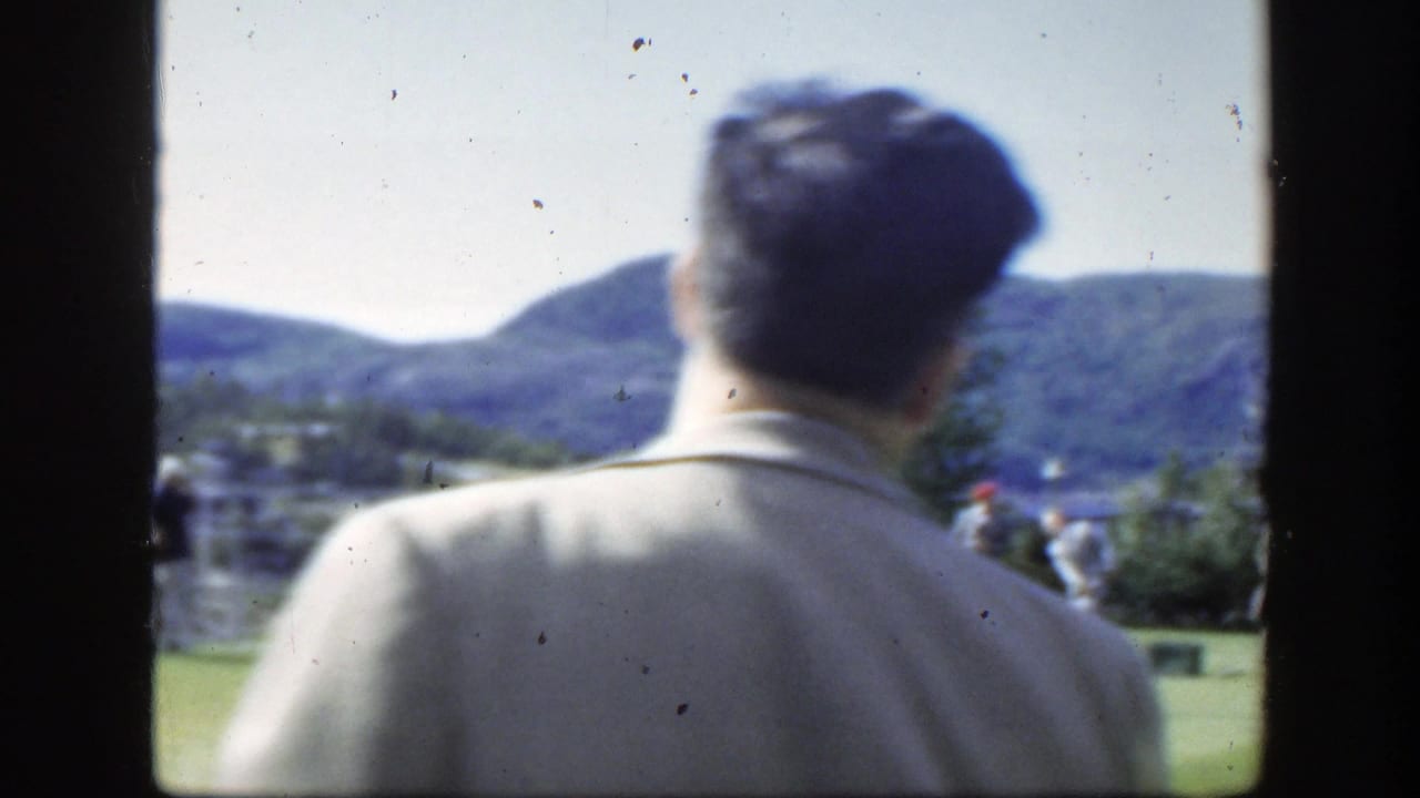 Man in a light suit seen from behind on a lawn with hills beyond.