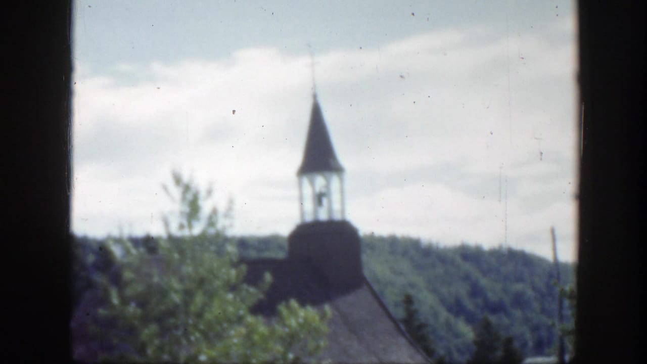 White church roof and steeple seen beyond trees with hills behind.