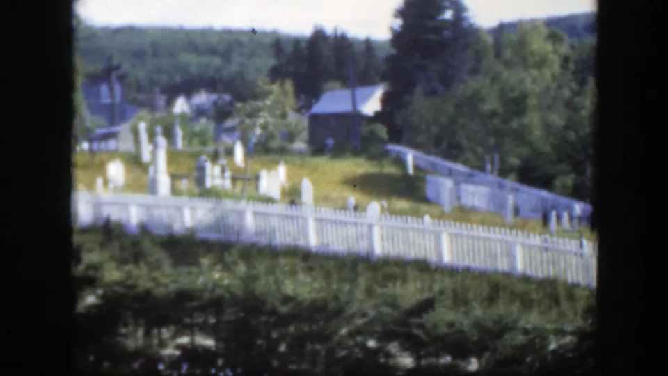 The final frame shows the Montreal-area cemetery from farther back, with white fencing, headstones, trees, and distant rural buildings.