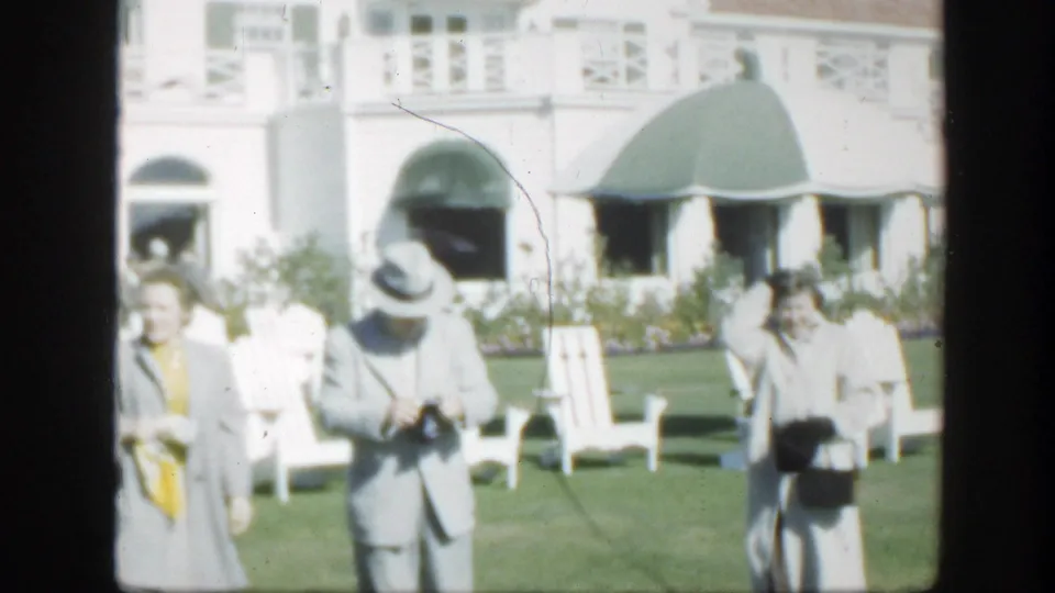 Older adults continue across the lawn outside the Montreal building, with white chairs, a green awning, and soft 8mm color visible.